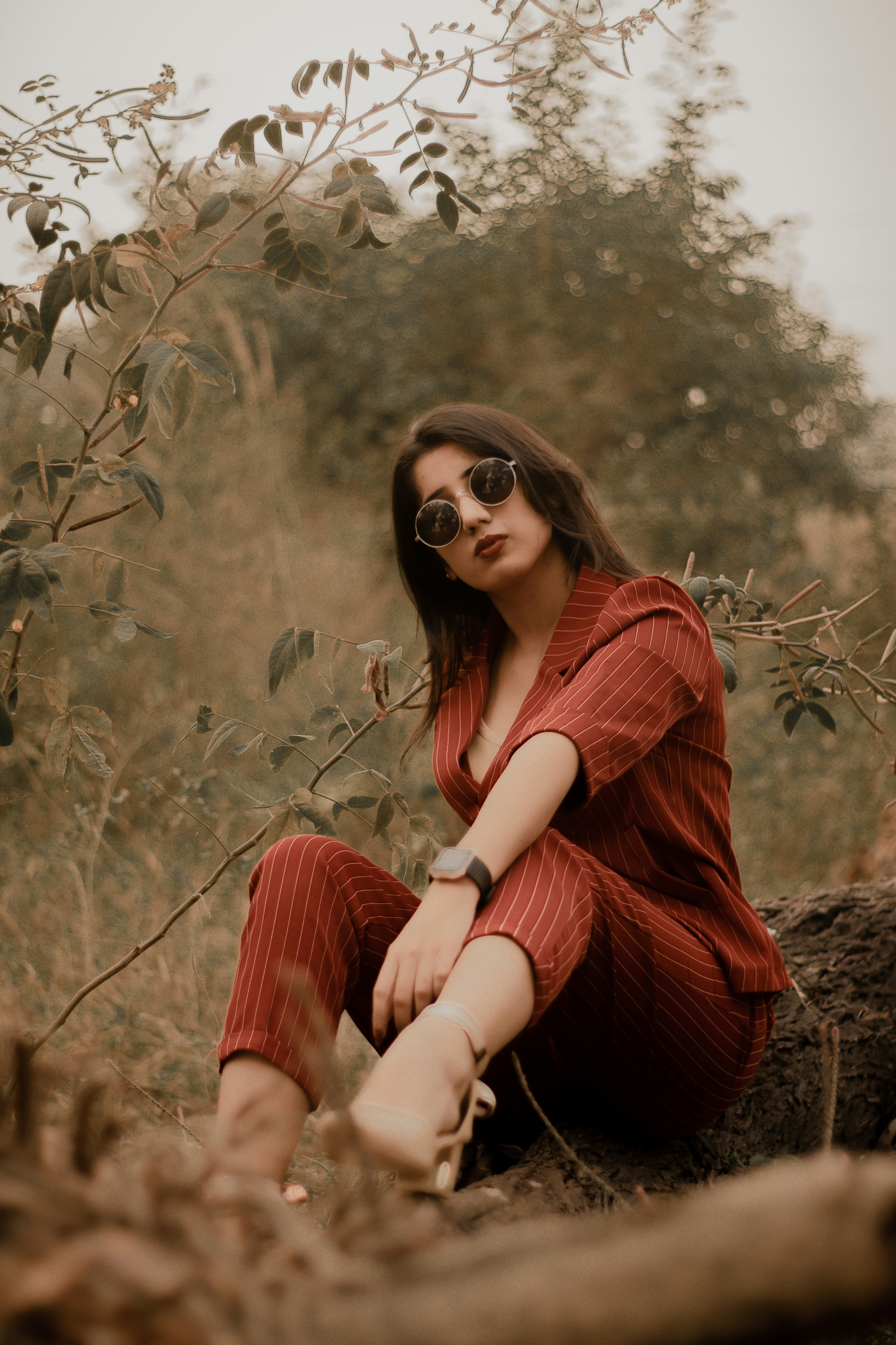 woman in red long sleeve shirt and black sunglasses sitting on brown grass field during daytime